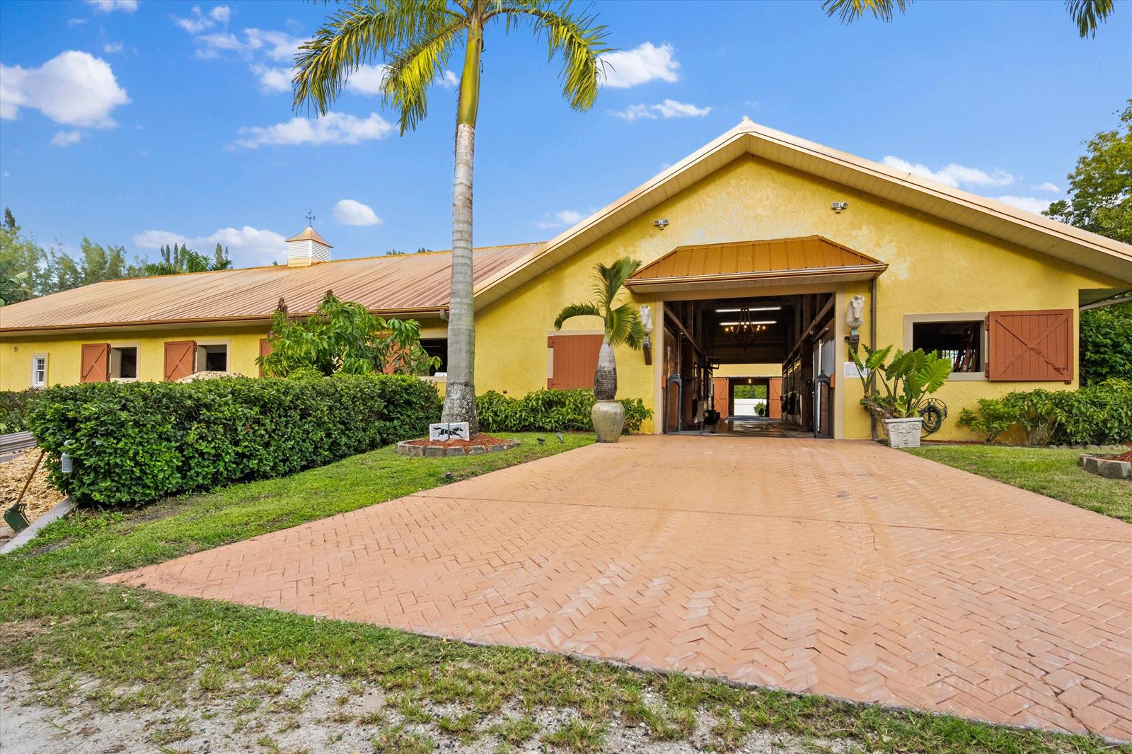 A yellow barn with a metal roof and a brick driveway under a blue sky — 11861 Hawk Hollow, Wellington FL 33449, WELLINGTON, FL