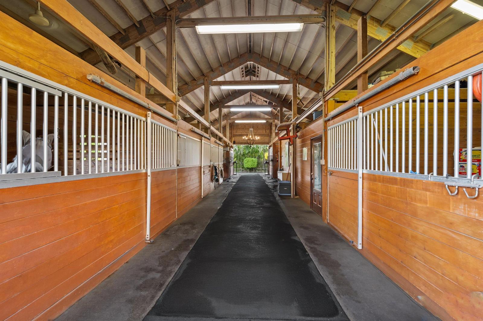 A horse stable aisle features wooden stalls with metal grates and a black rubber floor — 11861 Hawk Hollow, Wellington FL 33449, WELLINGTON, FL