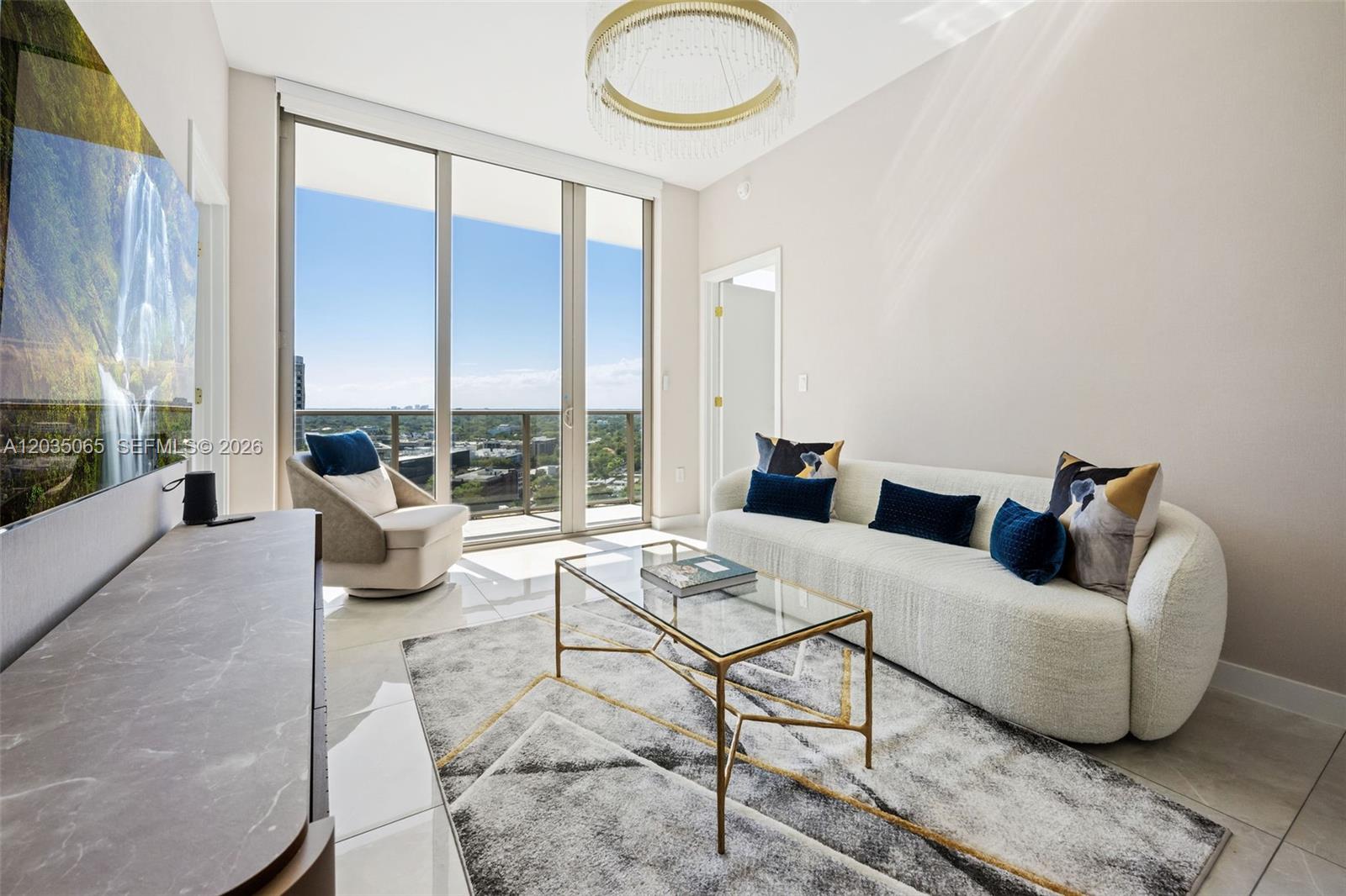 A modern living room features a white curved sofa, glass coffee table, and floor-to-ceiling windows — 2678 Tigertail Ave # 1705, Miami FL 33133, MIAMI, FL
