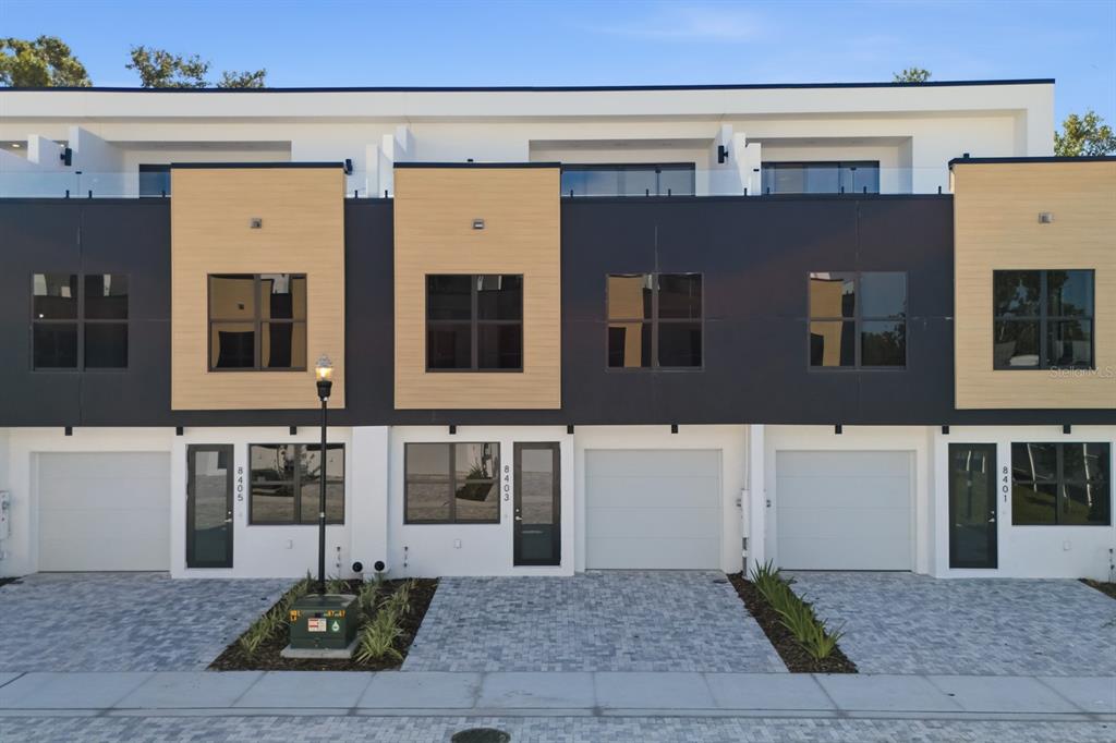 A row of modern townhouses features light wood-tone accents, dark panels, and white garage doors — 8405 MODANO PLACE, TAMPA, FL