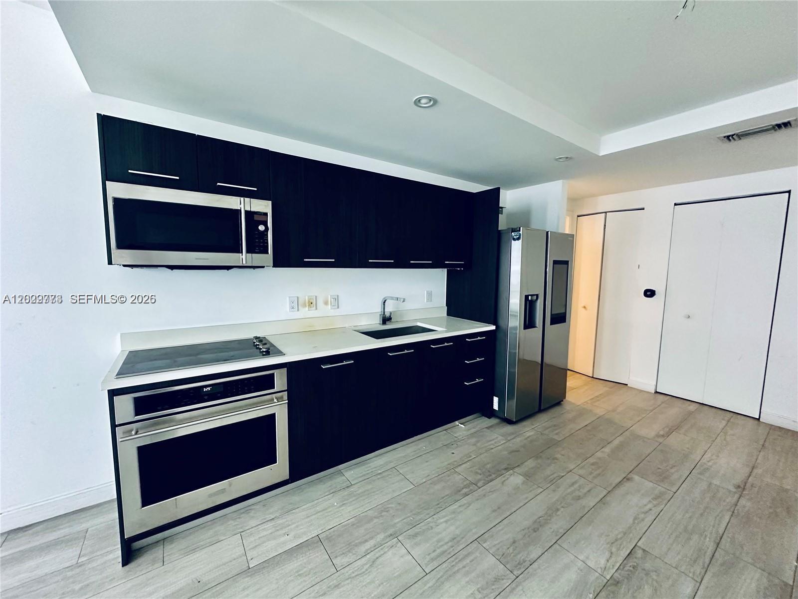A modern kitchen features dark wood cabinets, stainless steel appliances, and light-colored tile flooring — 55 SW 9th St # 3409, Miami FL 33130, MIAMI, FL