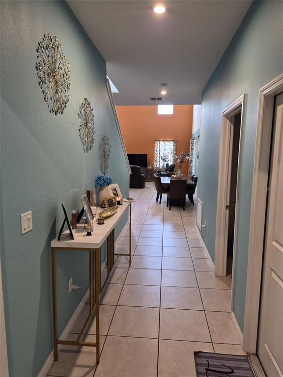 A hallway with light blue walls and tile flooring leads to an open-concept dining area — 1490 FLATWOOD STREET, ST CLOUD, FL