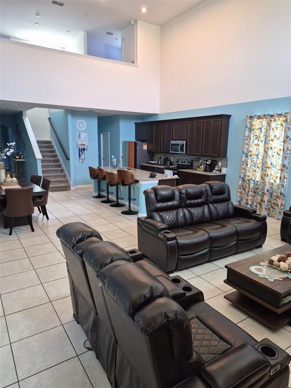 An open-concept living room and kitchen feature dark leather furniture, tile floors, and high ceilings — 1490 FLATWOOD STREET, ST CLOUD, FL