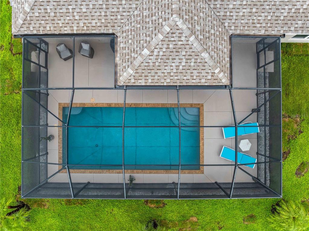 An aerial view of a rectangular swimming pool enclosed by a screened lanai with lounge chairs — 7664 MERONI BOULEVARD, NORTH PORT, FL