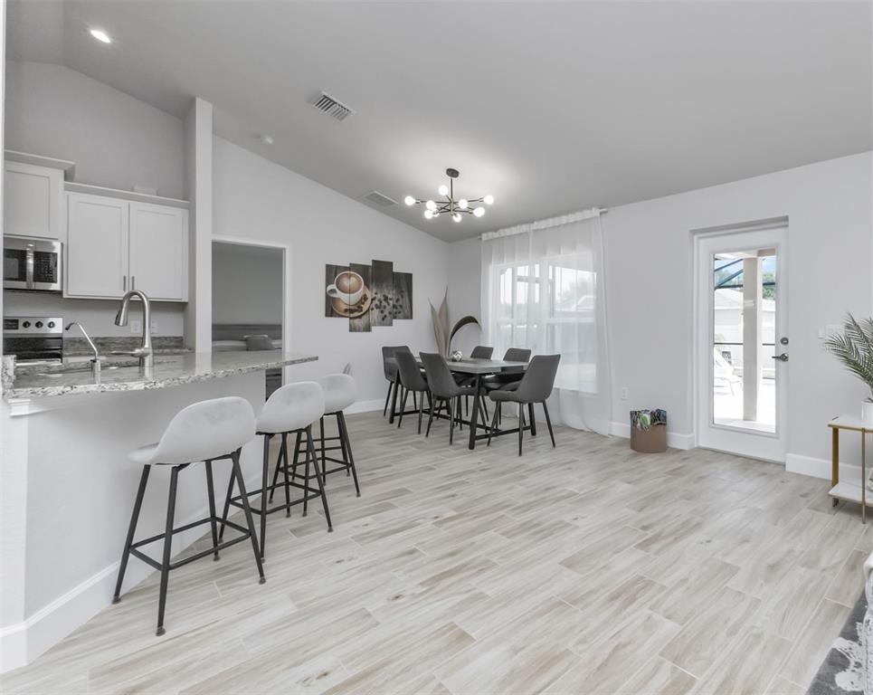 A kitchen with a breakfast bar and dining area features light wood-look tile flooring — 7664 MERONI BOULEVARD, NORTH PORT, FL