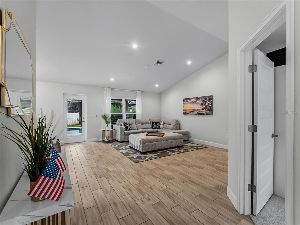 A living room features light wood-look tile flooring, a sectional sofa, and a glass door — 7664 MERONI BOULEVARD, NORTH PORT, FL