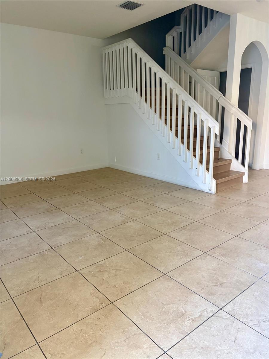 An empty room features beige tile flooring and a white wooden staircase — 9228 W 33rd Way # 9828, Hialeah FL 33018, HIALEAH, FL