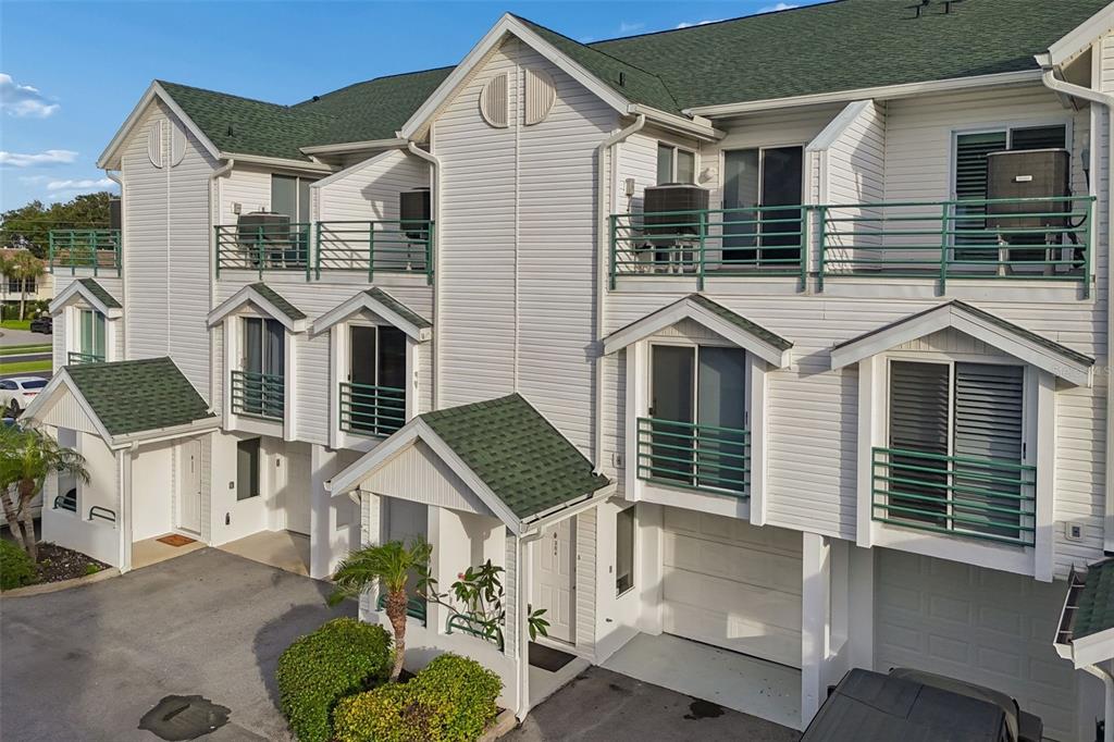 A multi-story townhouse exterior with white siding, green railings, and attached garages — 320 ISLAND WAY UNIT 304, CLEARWATER BEACH, FL