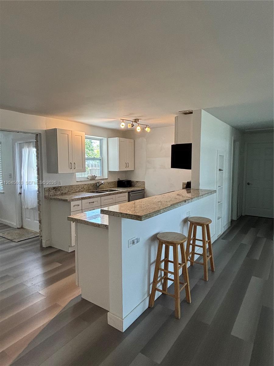 A kitchen features white cabinets, granite countertops, a breakfast bar with stools, and wood-look flooring — 5809 Sullivan Rd, Jupiter FL 33458, JUPITER, FL