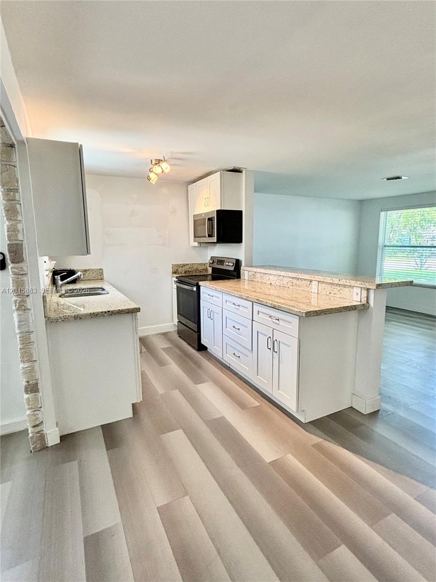 A kitchen features white cabinets, granite countertops, stainless steel appliances, and light wood-look flooring — 5809 Sullivan Rd, Jupiter FL 33458, JUPITER, FL