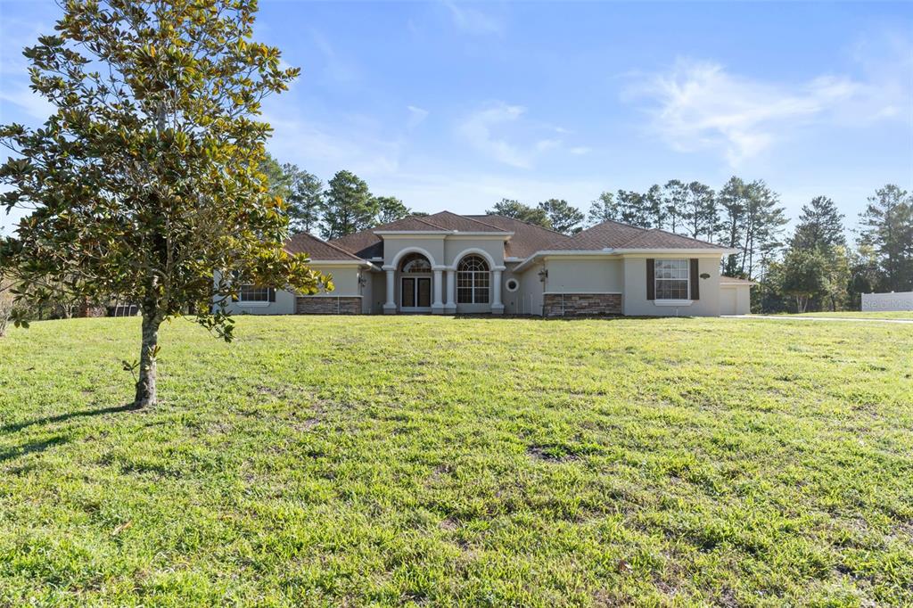 A single-story house with a beige exterior and arched windows sits on a grassy lot — 10130 LAZY DAYS COURT, WEEKI WACHEE, FL