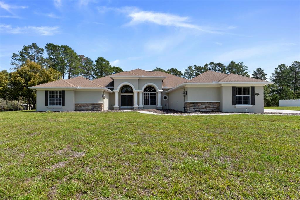 A single-story house with a tan stucco exterior, stone accents, and a brown shingled roof — 10130 LAZY DAYS COURT, WEEKI WACHEE, FL