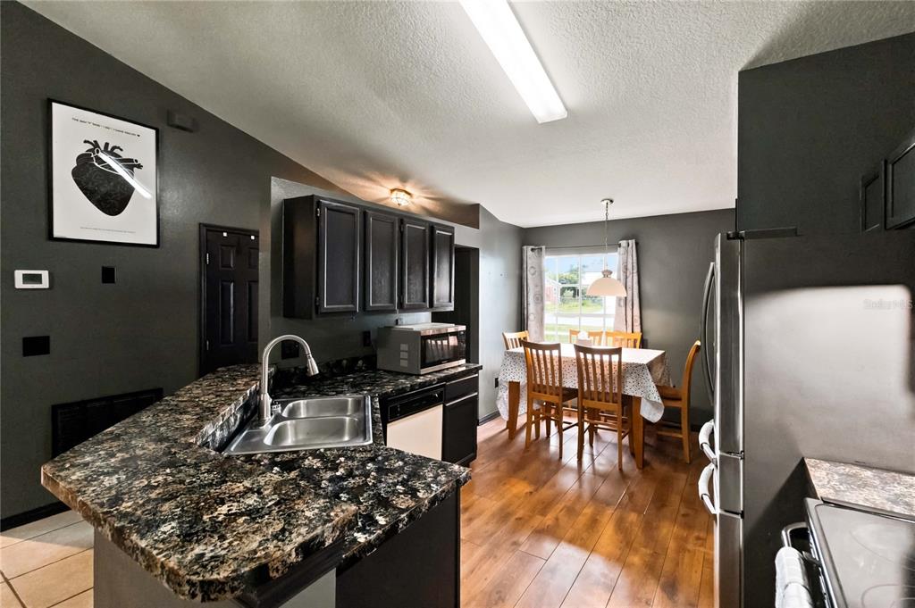 A kitchen with dark cabinets, granite countertops, and an adjacent dining area with wood floors — 677 SAGAMORE DRIVE, DELTONA, FL