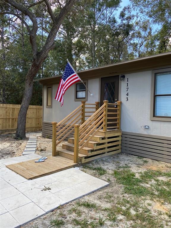 The exterior of a light-colored house features wooden stairs with railings and an American flag — 11743 PURDUE STREET, NEW PORT RICHEY, FL