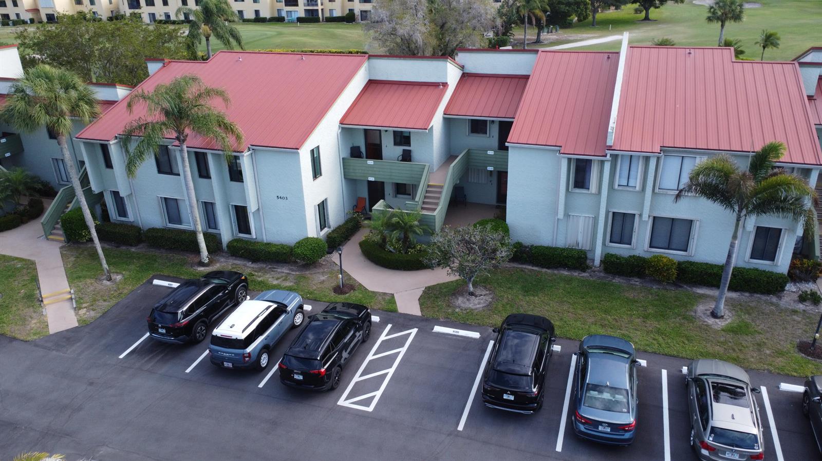 An aerial view shows a two-story apartment building with a red metal roof and parking — 5403 SE Miles Grant Road # H108, Stuart FL 34997, STUART, FL