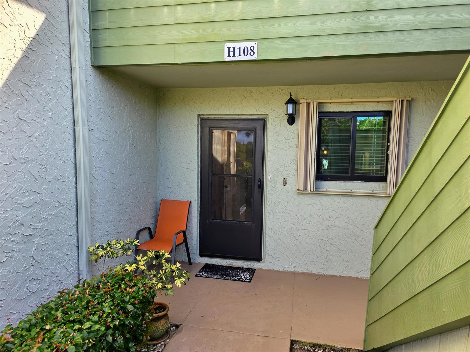 A ground-level apartment entrance features a dark screen door, an orange chair, and unit H108 — 5403 SE Miles Grant Road # H108, Stuart FL 34997, STUART, FL