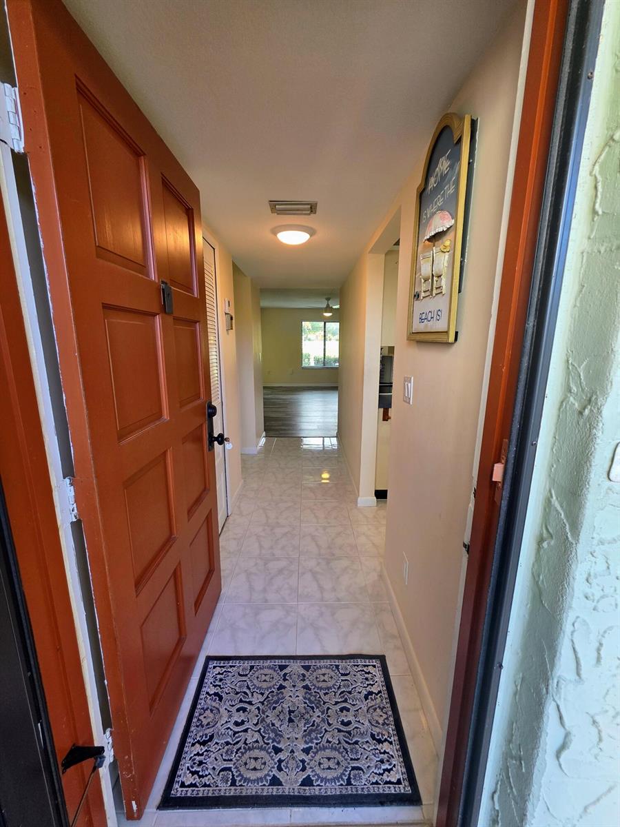 An open front door reveals a tiled entryway leading to a hallway and living area — 5403 SE Miles Grant Road # H108, Stuart FL 34997, STUART, FL