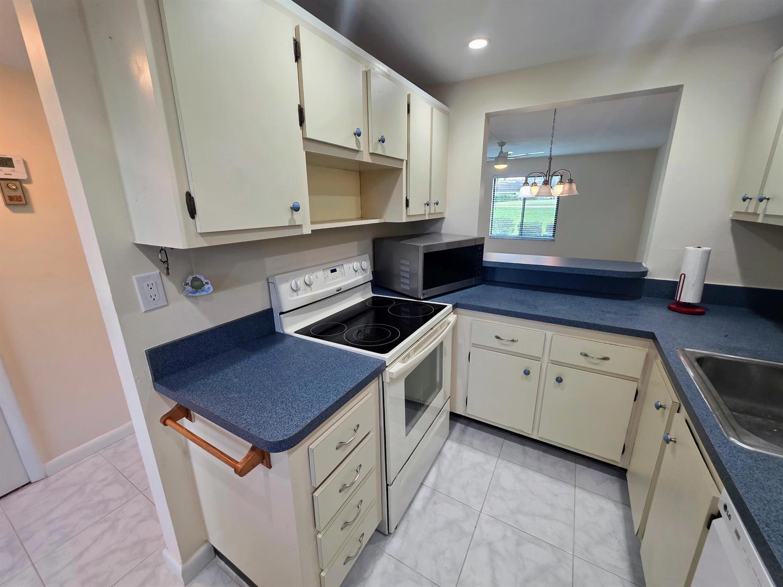 A kitchen features cream-colored cabinets, blue countertops, a white electric stove, and tile flooring — 5403 SE Miles Grant Road # H108, Stuart FL 34997, STUART, FL
