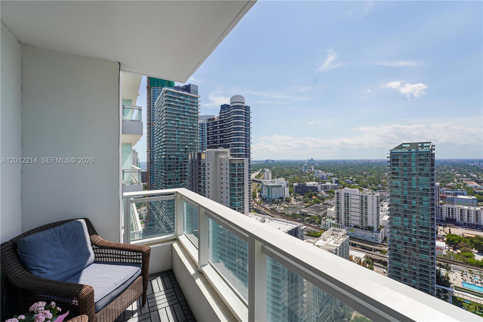 A high-rise balcony with a wicker chair overlooks a dense urban cityscape — 1080 Brickell Ave # 3607, Miami FL 33131, MIAMI, FL