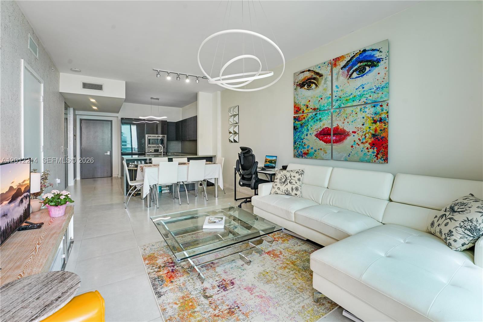 A modern living room features a white sectional sofa, glass coffee table, and colorful wall art — 1080 Brickell Ave # 3607, Miami FL 33131, MIAMI, FL