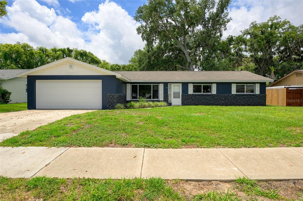 A single-story house with dark blue siding, stone accents, and a white garage door — 110 CAMBRIDGE DRIVE, PORT ORANGE, FL