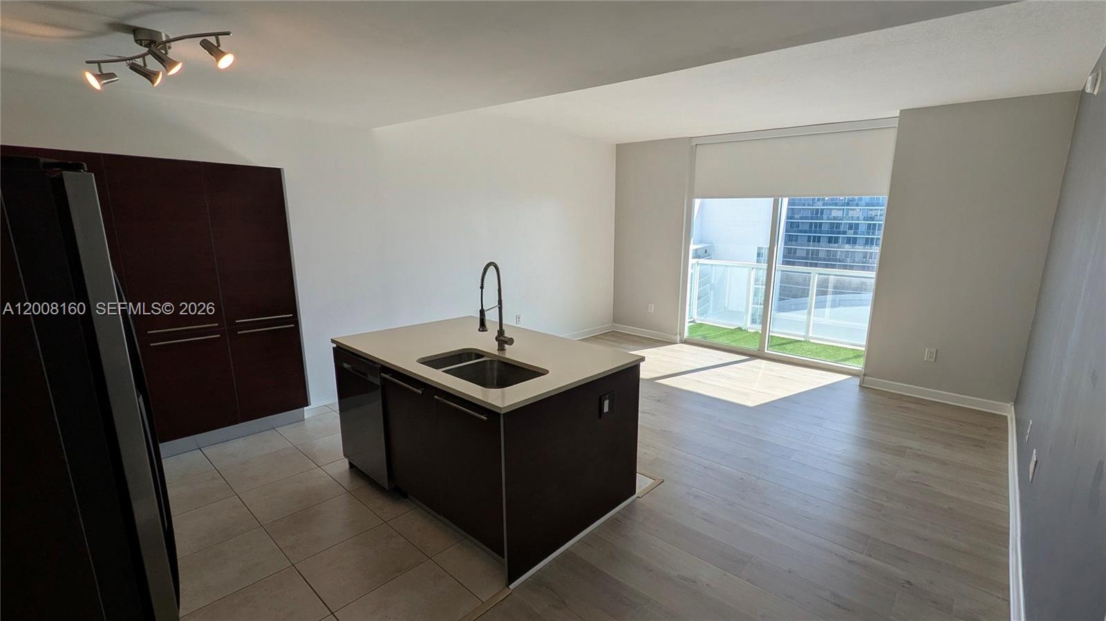 A modern kitchen features a dark wood island with a sink and light-colored flooring — 1900 N Bayshore Dr # 4007, Miami FL 33132, MIAMI, FL