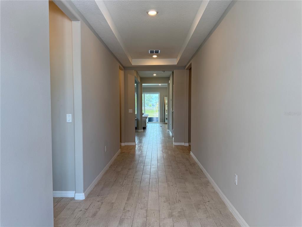 A long hallway with light wood-look tile flooring leads toward a bright living area — 3329 ORANGE ROSE LOOP, APOPKA, FL