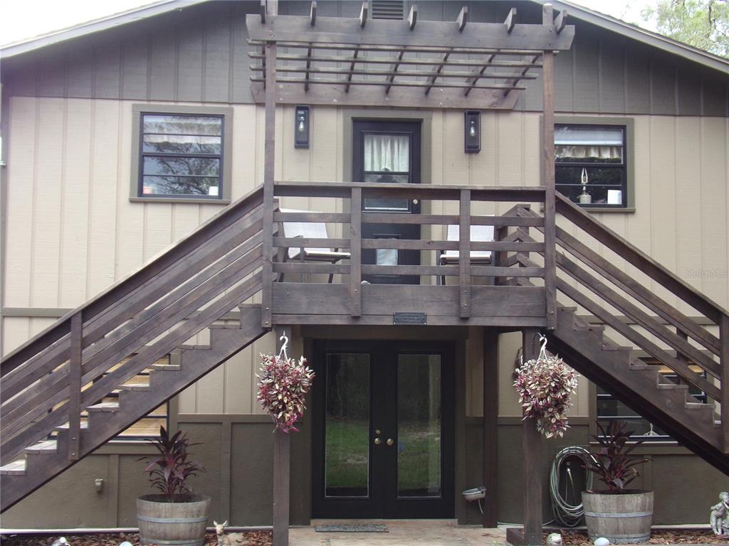 A two-story house exterior features a wooden staircase leading to an upper deck with a pergola — 33068 ROUND TABLE ROAD, DADE CITY, FL