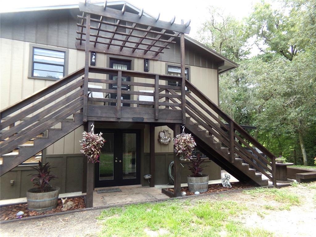 A two-story house exterior features a wooden staircase leading to an upper deck with a pergola — 33068 ROUND TABLE ROAD, DADE CITY, FL