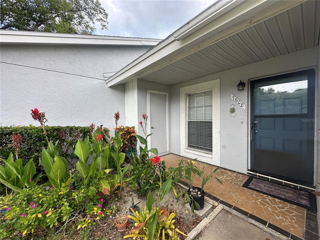 The front entrance features a covered porch, a blue storm door, and a landscaped garden — 7608 DANUBE DRIVE UNIT B, HUDSON, FL