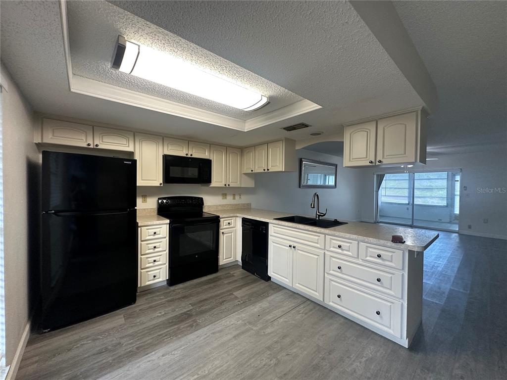 A kitchen features white cabinets, black appliances, and gray wood-look flooring — 7608 DANUBE DRIVE UNIT B, HUDSON, FL