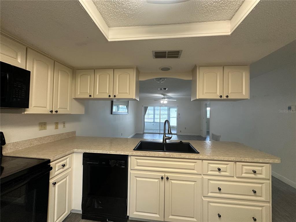 A kitchen with off-white cabinets, a black dishwasher, and a sink overlooking a living area — 7608 DANUBE DRIVE UNIT B, HUDSON, FL