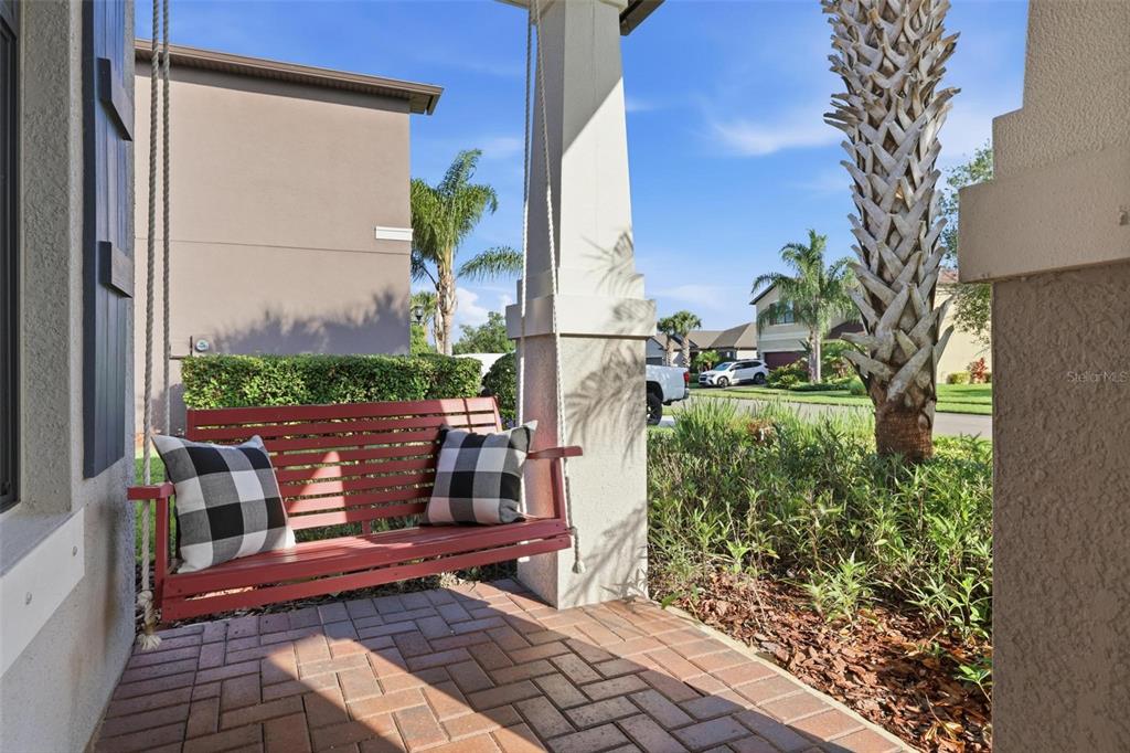 A red porch swing with plaid pillows sits on a brick-paved front porch — 2583 MARTON OAK BOULEVARD, NORTH PORT, FL