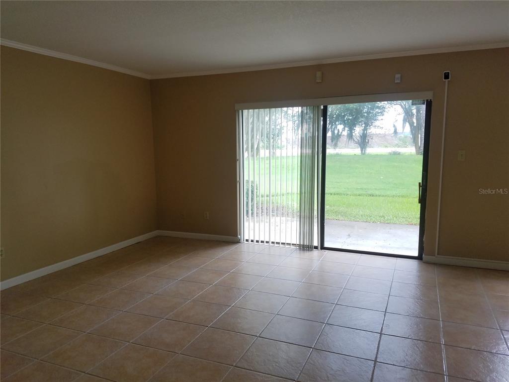 An empty room with tan walls, tiled flooring, and a sliding glass door to the outside — 5421 VINELAND ROAD UNIT 6A, ORLANDO, FL