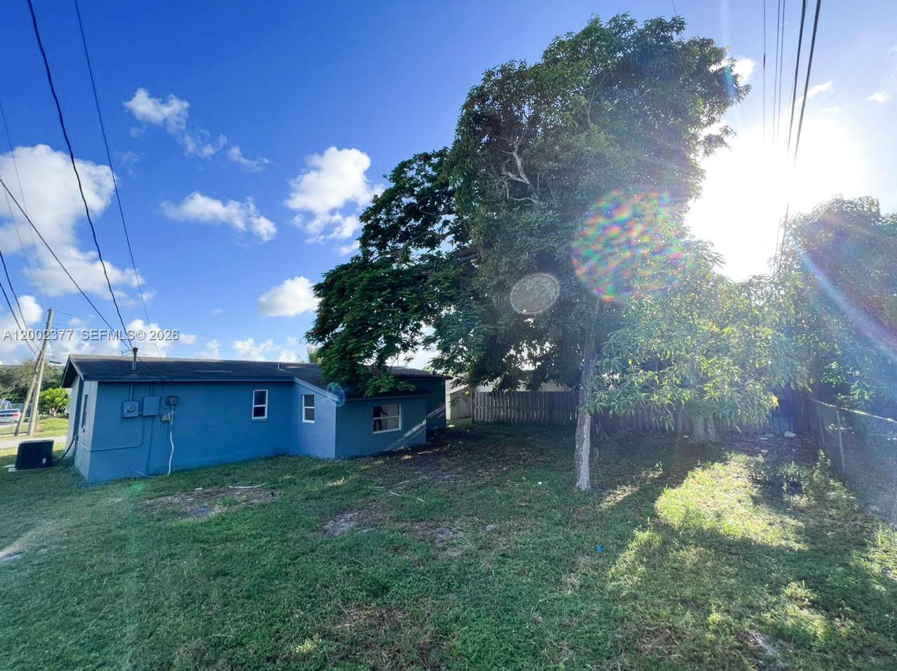 A blue house exterior features a large tree in the backyard under a sunny sky — 3461 NW 17th St, Lauderhill FL 33311, LAUDERHILL, FL