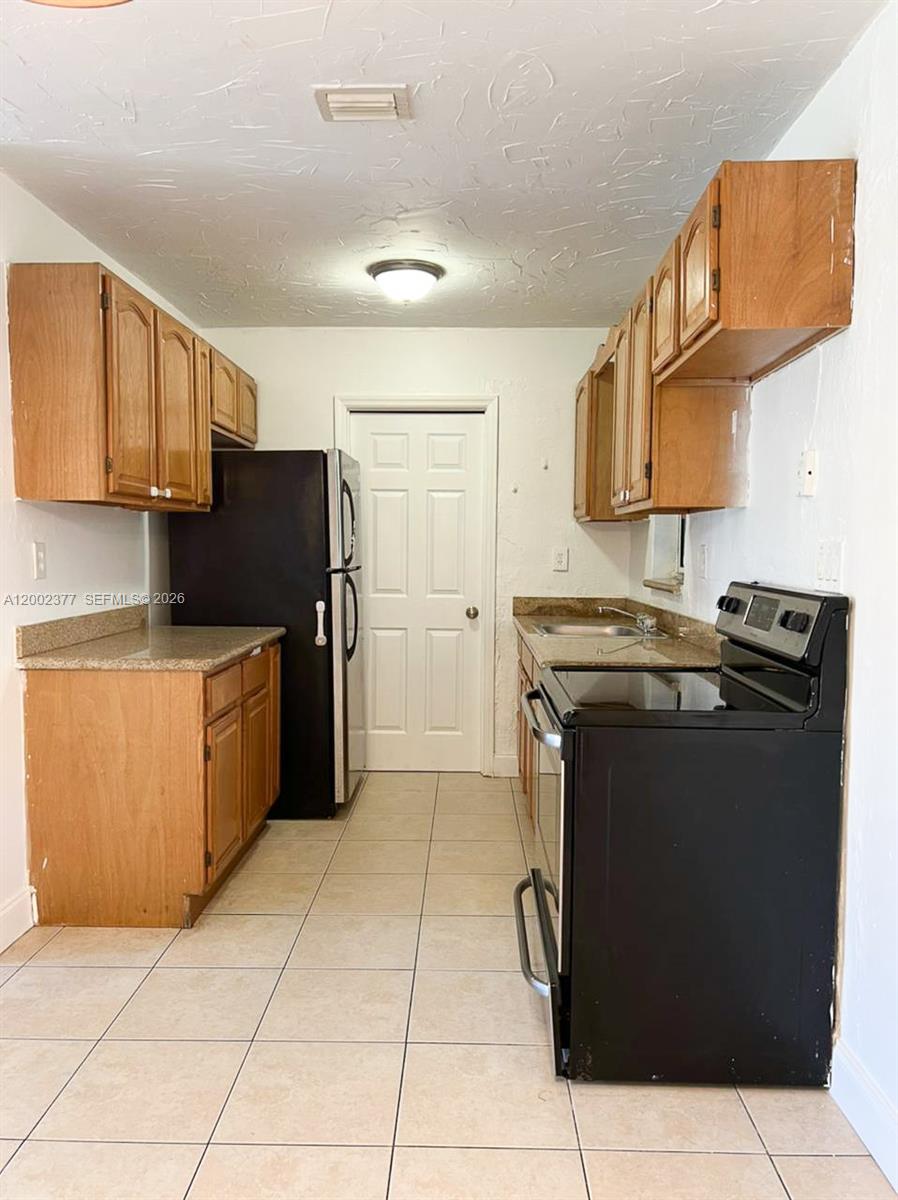 This galley-style kitchen features wood cabinets, black appliances, granite countertops, and light tile flooring — 3461 NW 17th St, Lauderhill FL 33311, LAUDERHILL, FL
