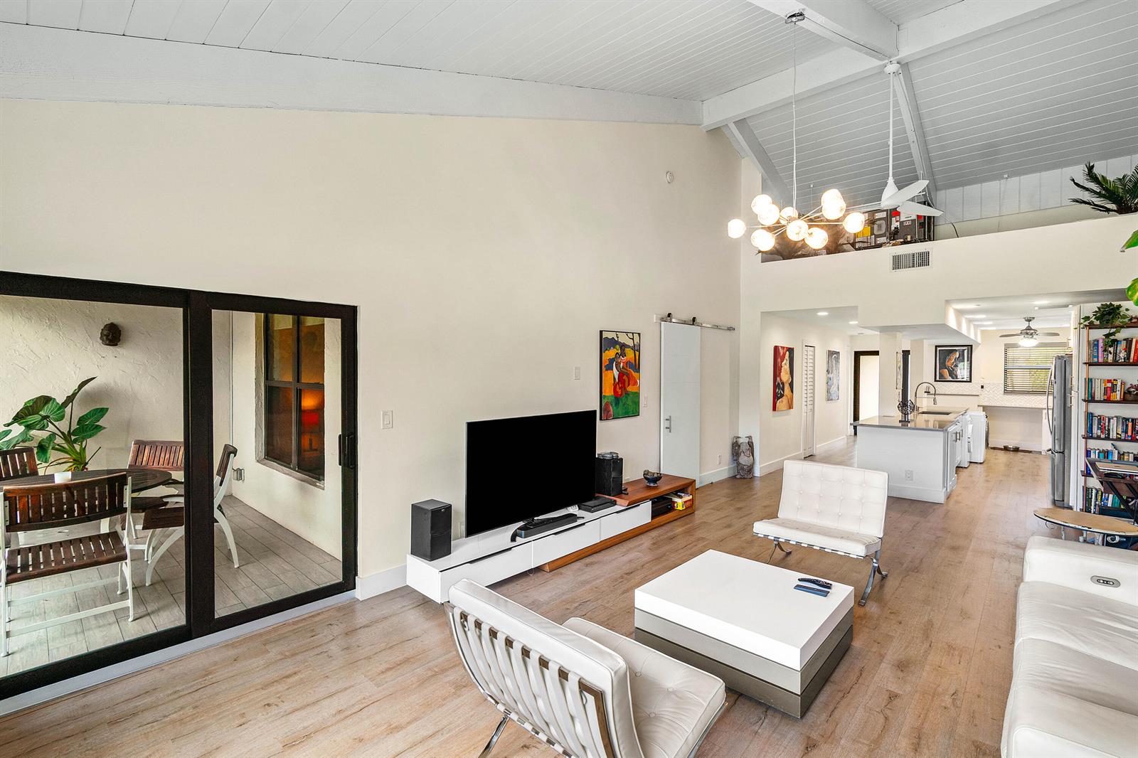 A bright living room features vaulted ceilings, hardwood floors, modern furniture, and an adjacent patio — 830 Greensward Court # h, Delray Beach FL 33445, DELRAY BEACH, FL
