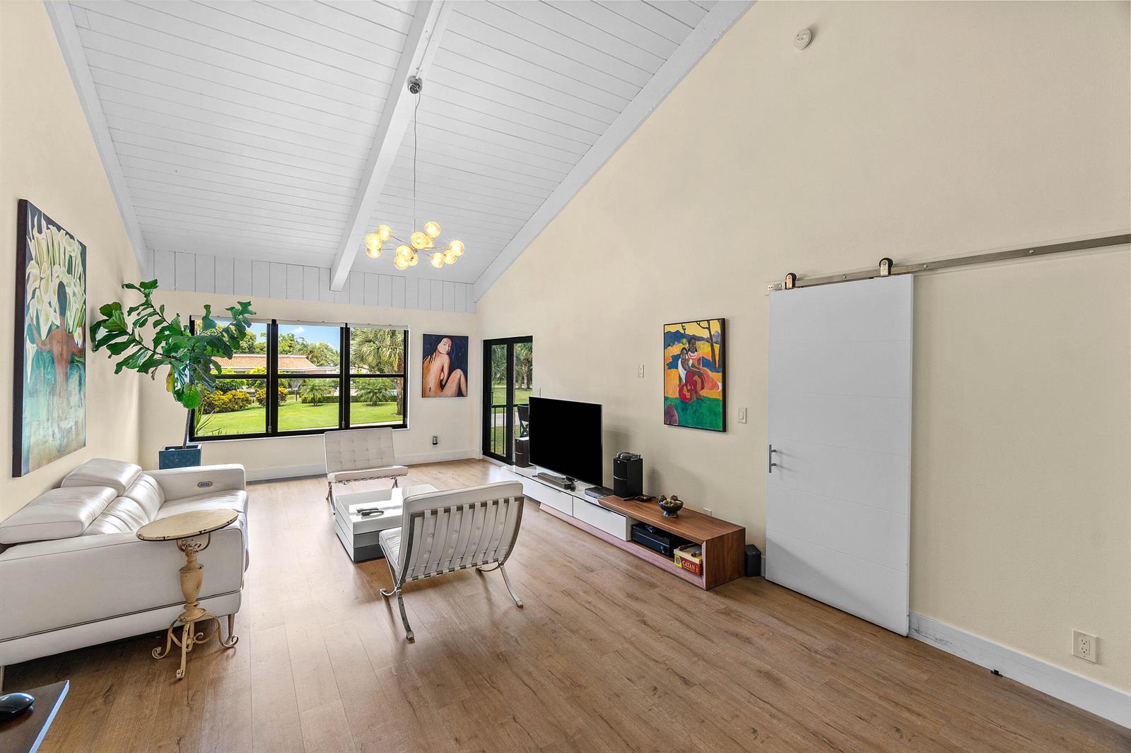 A living room features a vaulted ceiling, white leather furniture, a barn door, and large windows — 830 Greensward Court # h, Delray Beach FL 33445, DELRAY BEACH, FL