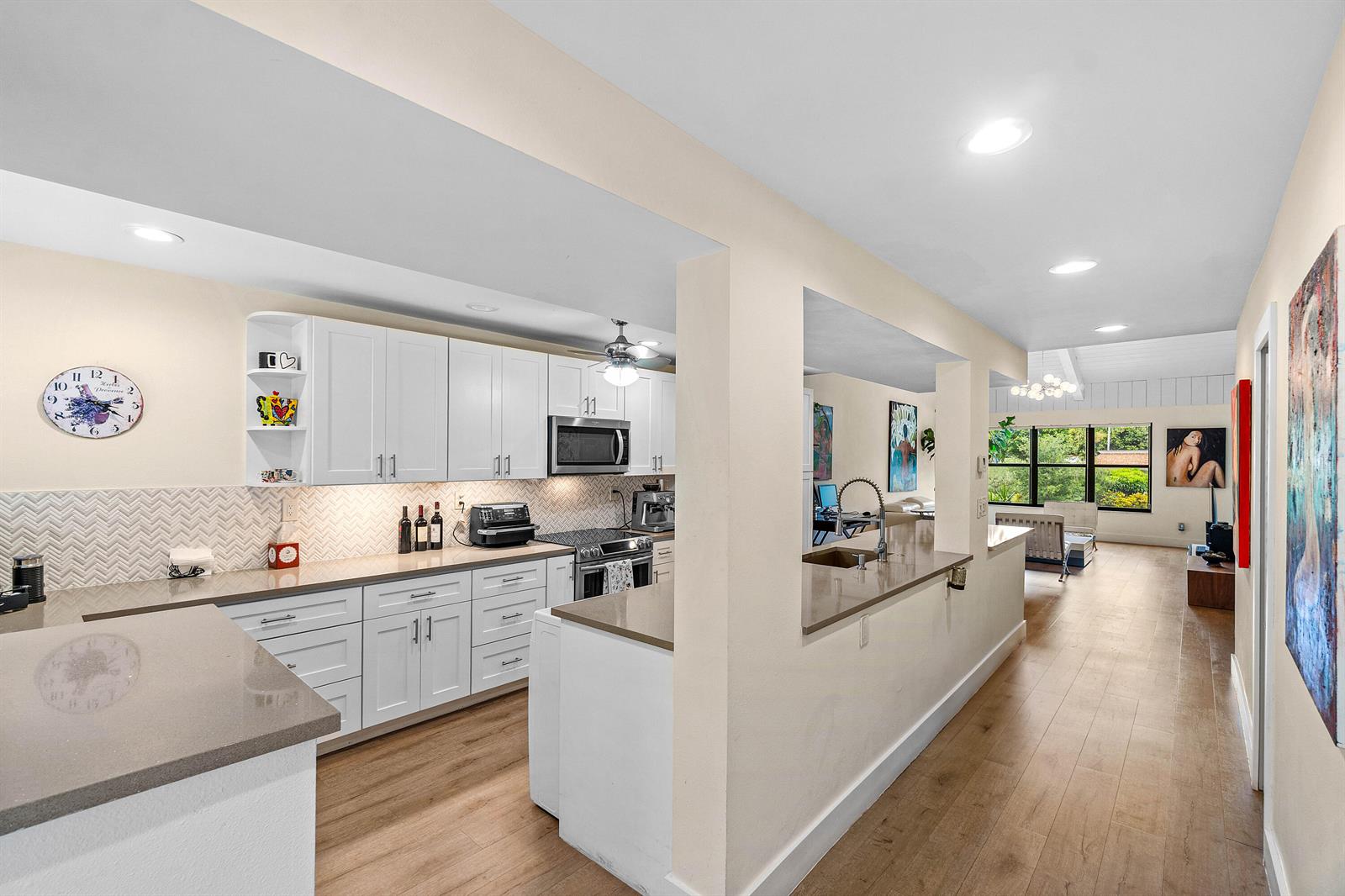 A kitchen with white cabinets and quartz countertops opens into a living area with wood floors — 830 Greensward Court # h, Delray Beach FL 33445, DELRAY BEACH, FL