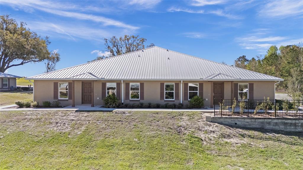 A single-story duplex with a metal roof, tan stucco exterior, and a front lawn — 7462 NW 44TH LANE, OCALA, FL