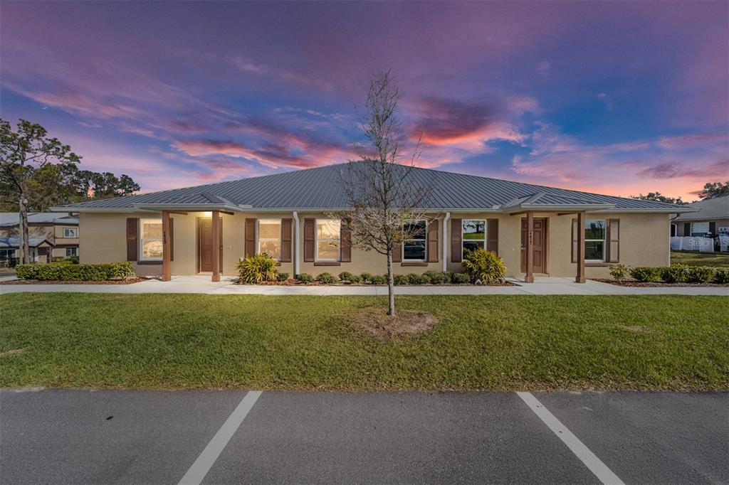 A single-story duplex building with a metal roof and tan stucco exterior at sunset — 7462 NW 44TH LANE, OCALA, FL