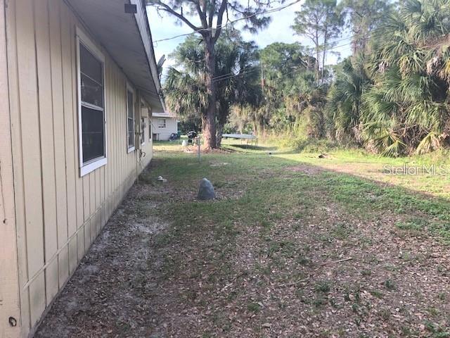 The side exterior of a tan house features vertical siding and windows overlooking a yard — 232 BAMBOO DRIVE UNIT A, PORT CHARLOTTE, FL