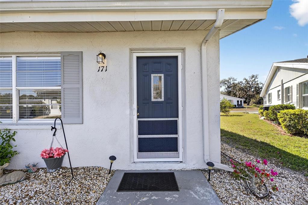 A white exterior wall features a blue front door with a screen door and shutters — 301 ANDOVER PLACE S UNIT 171, SUN CITY CENTER, FL