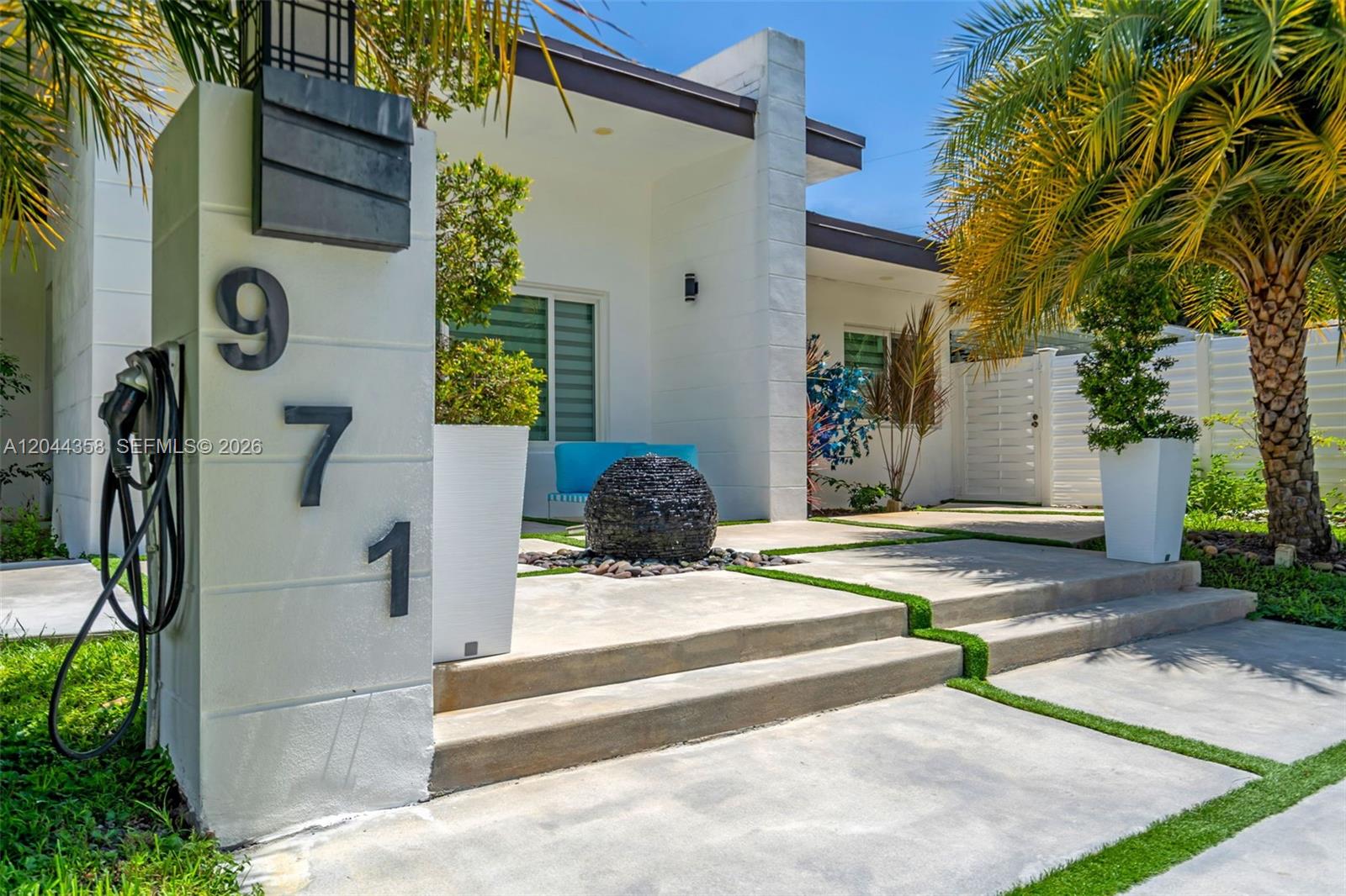 A modern house exterior features a white pillar with address numbers and a stone fountain — BISCAYNE PARK, FL