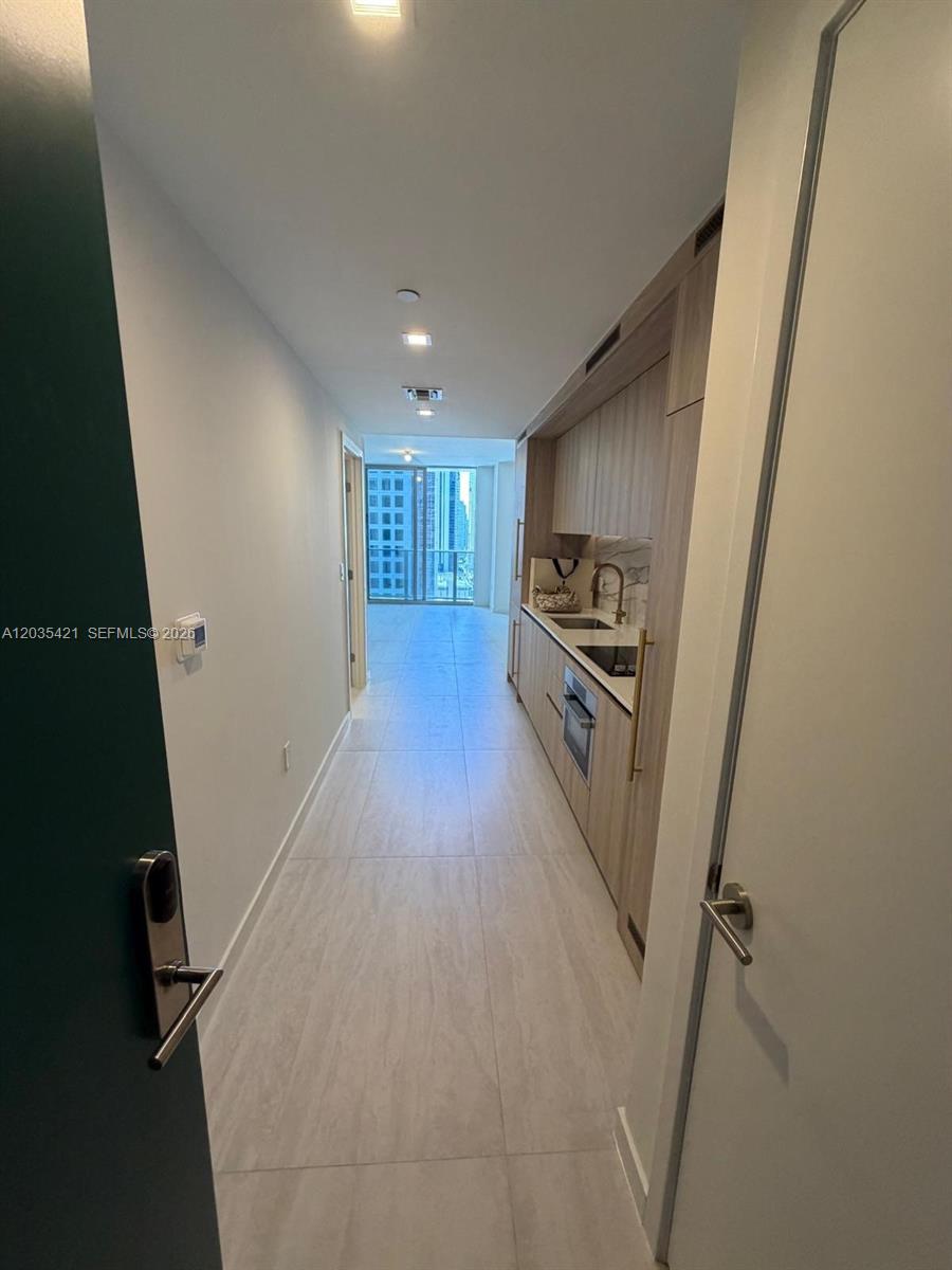A narrow hallway leads to a kitchen with light wood cabinetry and a balcony view — 77 SE 5th # 2512, Miami FL 33131, MIAMI, FL