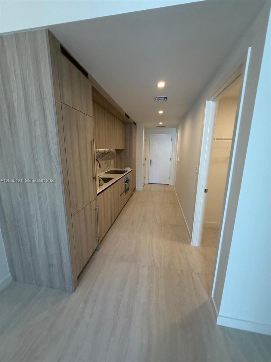 A narrow galley kitchen features light wood cabinetry, stainless steel appliances, and matching wood-look flooring — 77 SE 5th # 2512, Miami FL 33131, MIAMI, FL