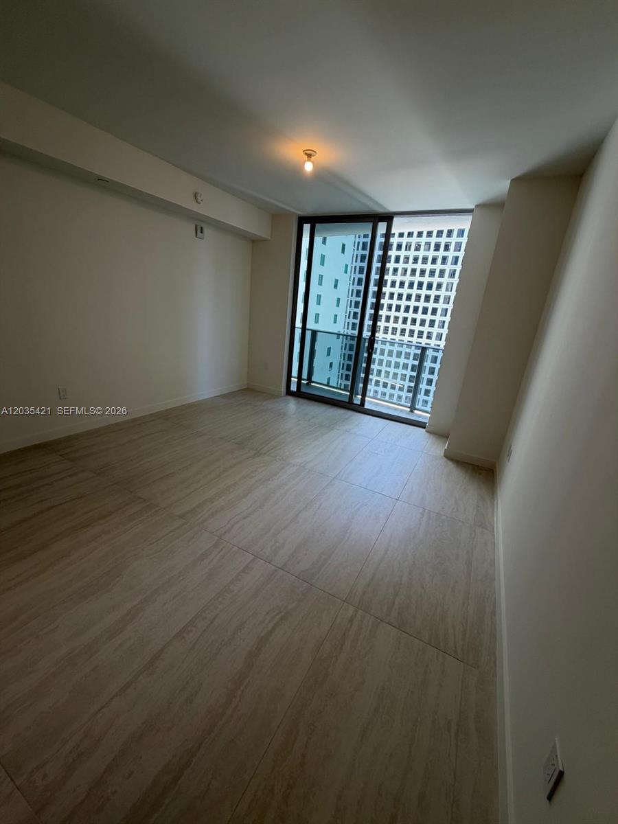 An empty room features large light-colored floor tiles, white walls, and a sliding glass door — 77 SE 5th # 2512, Miami FL 33131, MIAMI, FL