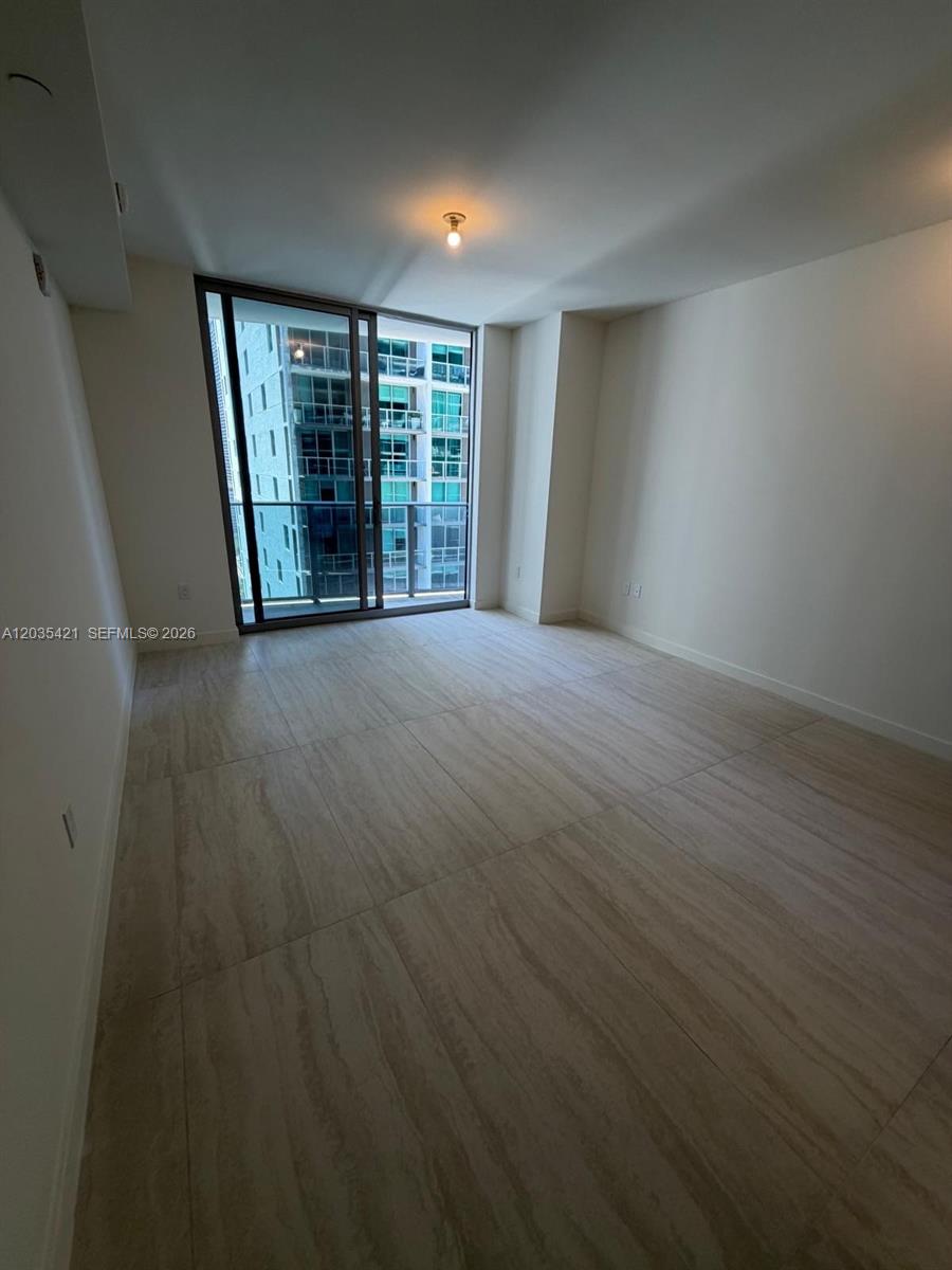 An empty room features large light-colored floor tiles, white walls, and a sliding glass door — 77 SE 5th # 2512, Miami FL 33131, MIAMI, FL