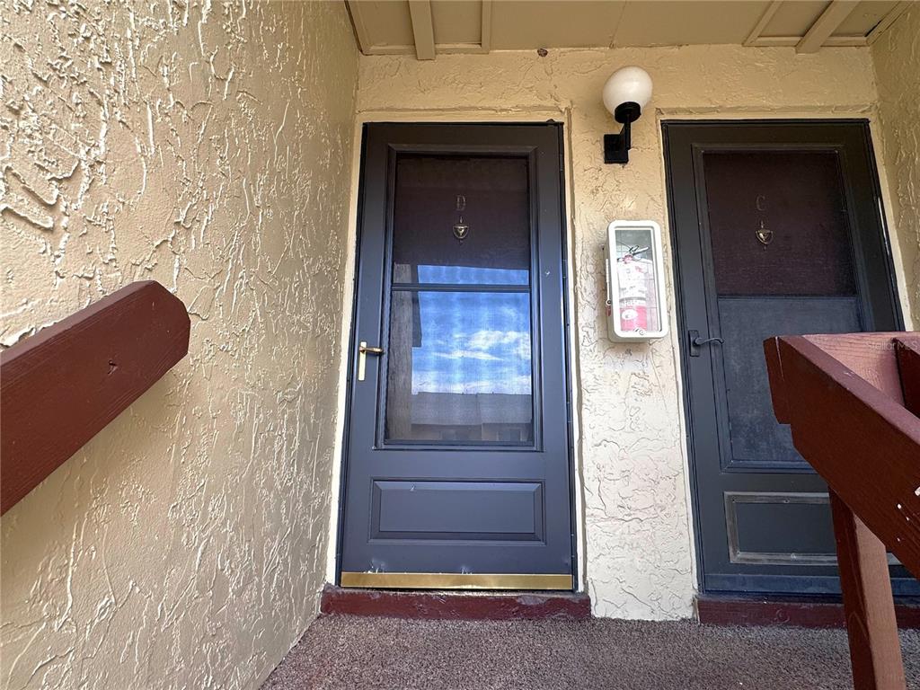 Two dark-framed screen doors with unit letters are set into a textured beige exterior wall — 4215 E BAY DRIVE UNIT 1602D, CLEARWATER, FL
