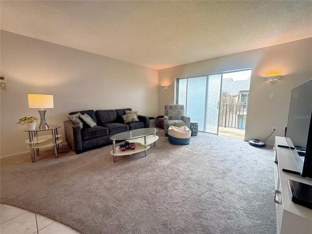 A living room features a dark sofa, glass coffee table, patterned armchair, and sliding glass doors — 4215 E BAY DRIVE UNIT 1602D, CLEARWATER, FL